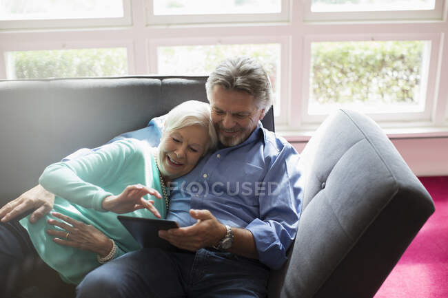 Glückliches Senioren-Paar kuschelt und nutzt digitales Tablet auf dem Sofa — Stockfoto