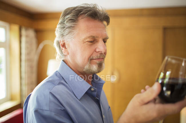 Старший мужчина пьет красное вино дома — стоковое фото