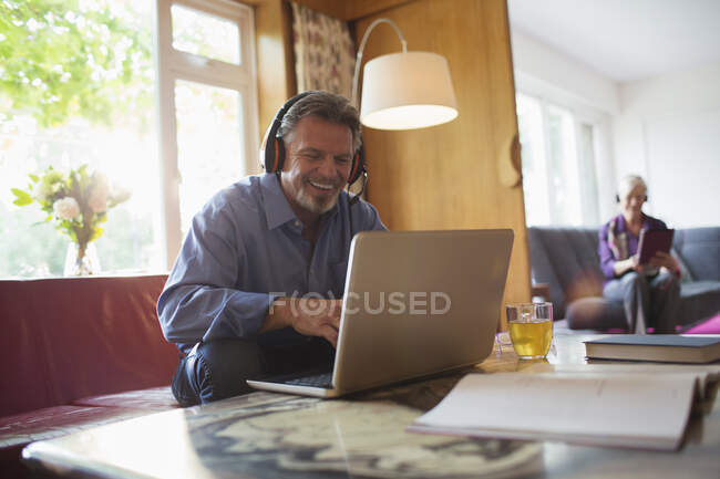 Heureux homme âgé avec écouteurs utilisant un ordinateur portable dans le salon — Photo de stock