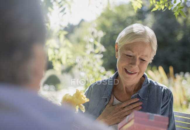 Счастливая пожилая женщина получает подарок от мужа на солнечном патио — стоковое фото