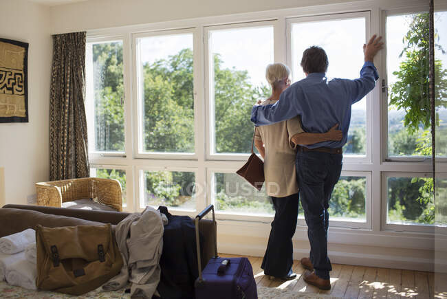 Affectueux couple de personnes âgées étreignant à la fenêtre de location de maison ensoleillée — Photo de stock