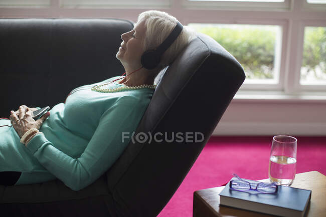 Donna anziana serena che ascolta musica con cuffie sul divano — Foto stock