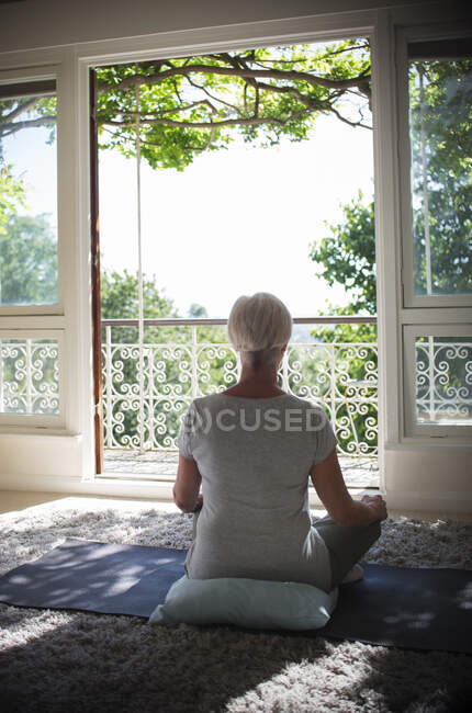 Serene senior woman meditating at tranquil summer balcony doorway — Stock Photo