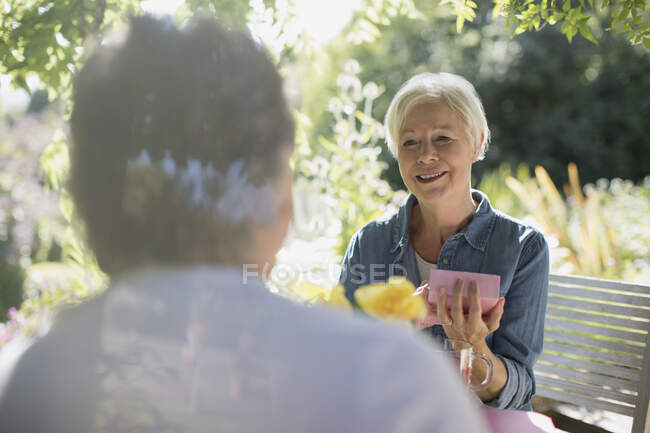Щаслива старша жінка відкриває подарунок від чоловіка на сонячному літньому патіо — стокове фото