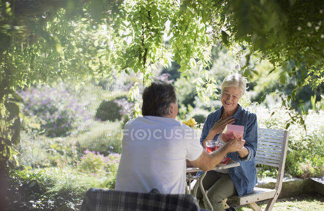 Happy senior woman opening gift from husband on summer patio — Stock Photo