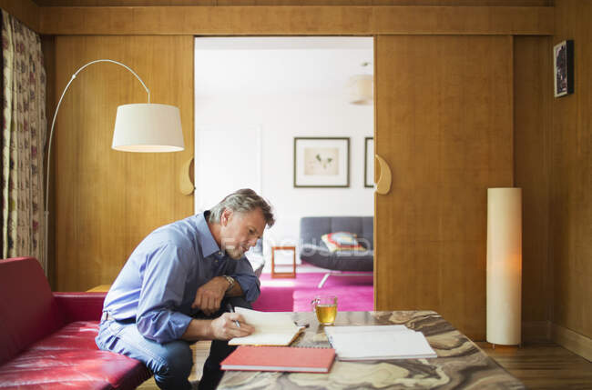 Homem sênior com caderno trabalhando na sala de estar — Fotografia de Stock