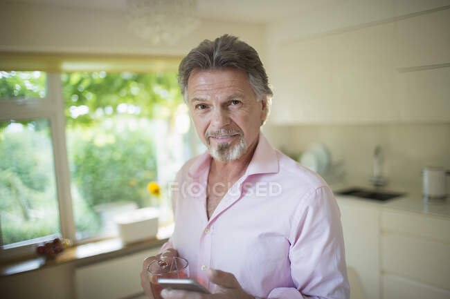 Portrait confident senior man with smart phone and tea in kitchen — Stock Photo
