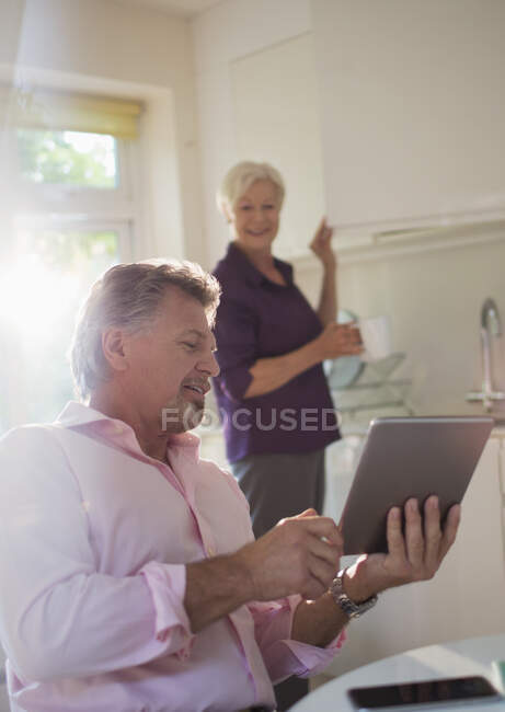 Старша пара з цифровим планшетом, що говорить на кухні — стокове фото
