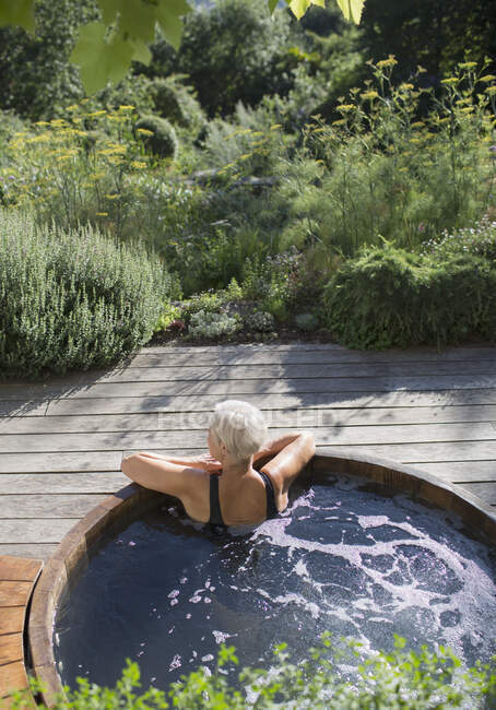 Старша жінка розслабляється в гарячій ванні на сонячному літньому патіо — стокове фото