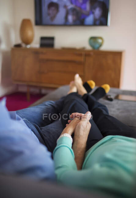 Couple affectueux tenant la main et regardant la télévision sur le canapé — Photo de stock