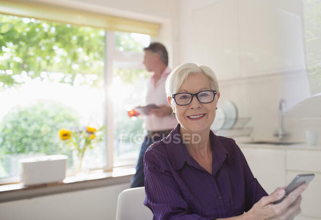 Портрет счастливой пожилой женщины с помощью смартфона на солнечной кухне — стоковое фото