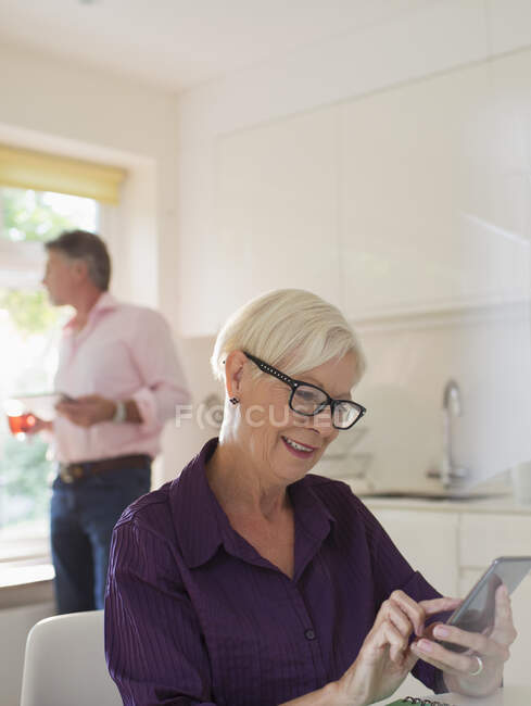 Mulher sênior usando telefone inteligente na cozinha — Fotografia de Stock