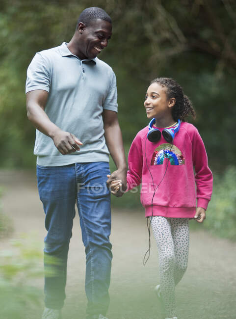 Feliz padre e hija tomados de la mano caminando por el sendero del parque - foto de stock