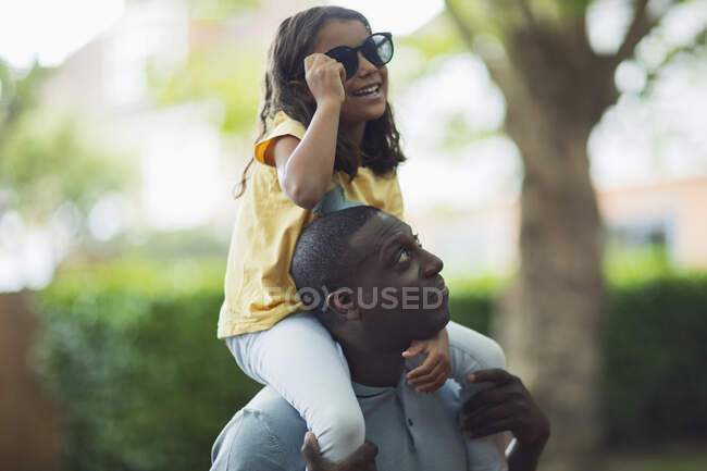 Father carrying daughter with sunglasses on shoulders — Stock Photo