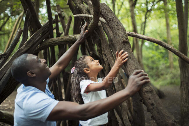 Padre e hija haciendo tipi con ramas en el bosque - foto de stock