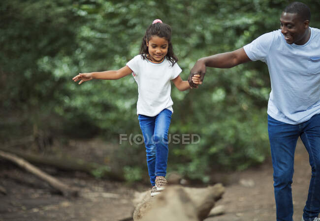 Father helping daughter balance on fallen log in woods — Stock Photo