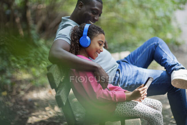 Padre e hija con auriculares y tableta digital en el banco del parque - foto de stock