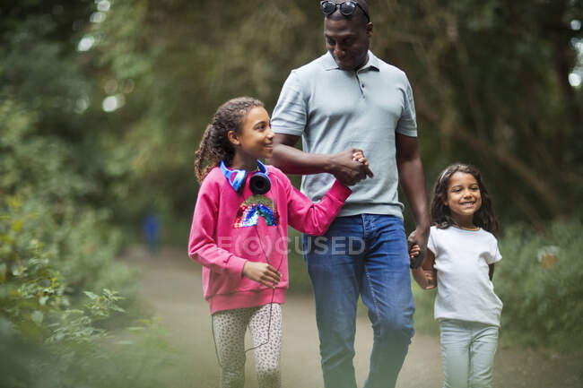 Feliz padre e hijas tomados de la mano caminando por el sendero del parque - foto de stock