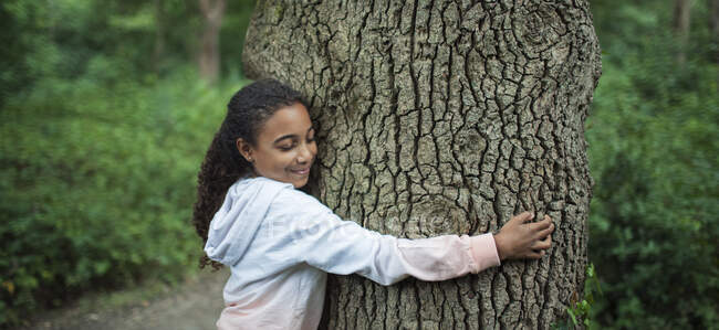 Спокойная девушка обнимает ствол дерева в лесу — стоковое фото
