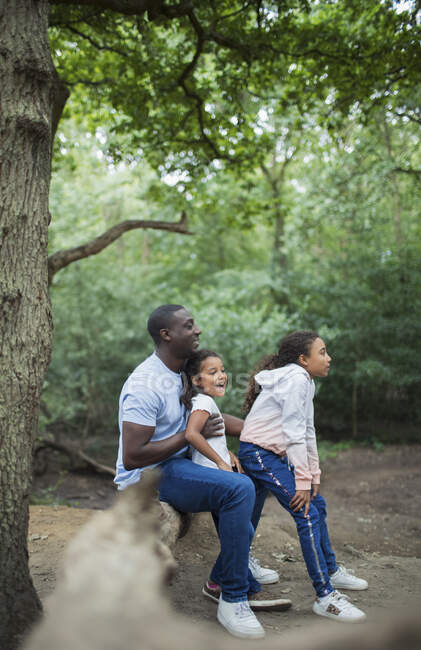 Happy father and daughters sitting on fallen log in woods — Stock Photo