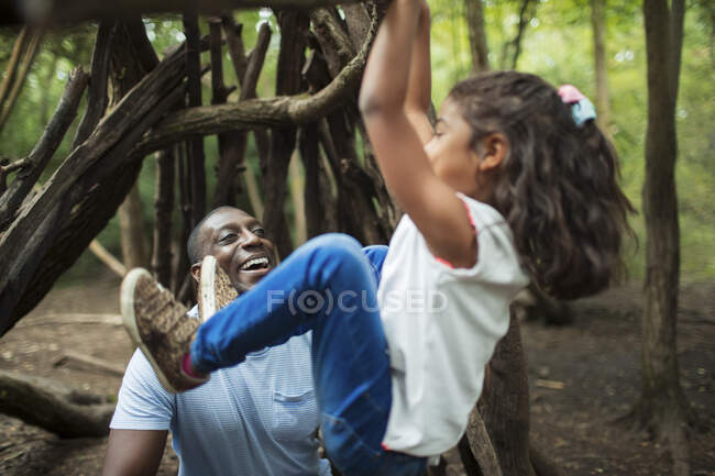 Father watching daughter hang from branch in woods — Stock Photo