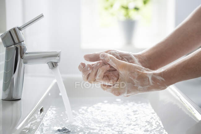 Close up teenage boy washing hands with soap and water at sink — Foto stock