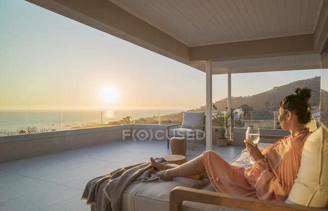 Woman enjoying white wine and sunset ocean view on luxury balcony — Fotografia de Stock
