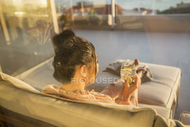 Женщина расслабляется с водой на солнечном диване патио — стоковое фото