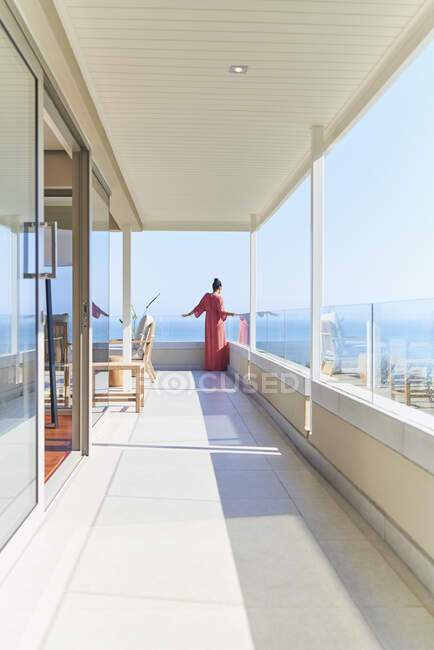 Frau in Kleid genießt sonnigen Meerblick vom Luxus-Balkon — Stockfoto