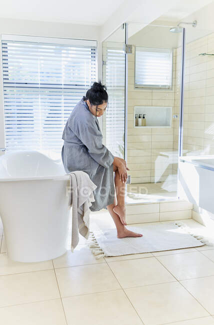 Donna in accappatoio toccare gamba in casa vetrina bagno interno — Foto stock