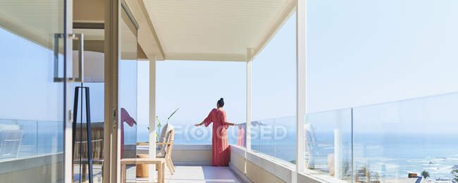 Femme en robe longue profitant d'une vue panoramique ensoleillée sur l'océan sur le balcon de luxe — Photo de stock