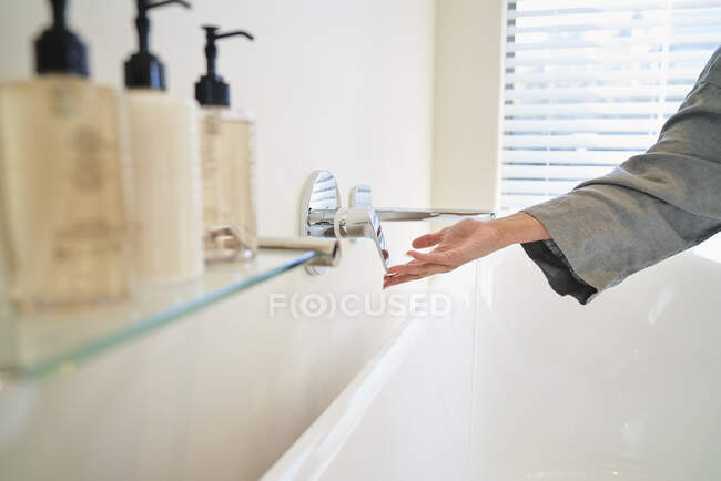 Mujer girando el grifo sobre la bañera en el baño - foto de stock