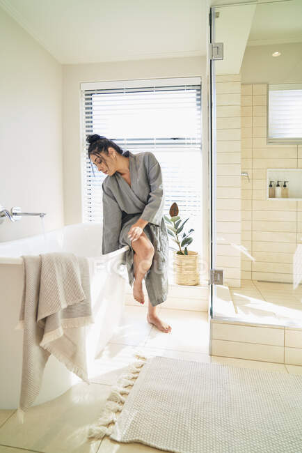 Frau im Bademantel bereitet Badewanne für Bad im sonnigen Badezimmer vor — Stockfoto