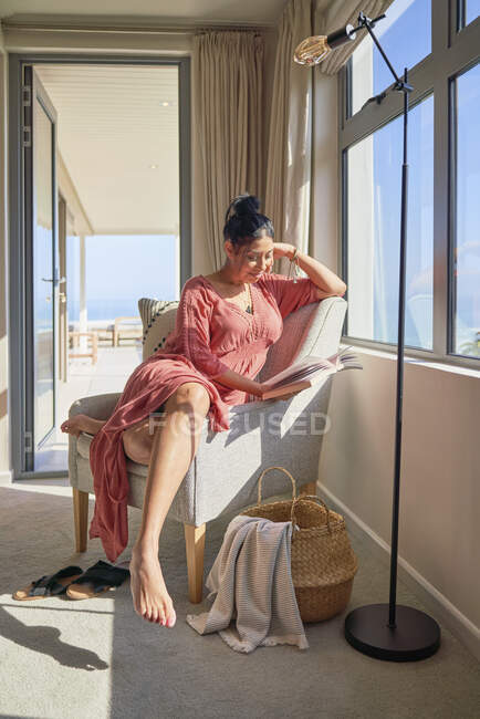 Mujer relajante y libro de lectura en ventana soleada - foto de stock