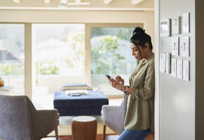 Mulher usando telefone inteligente por controles de automação residencial — Fotografia de Stock