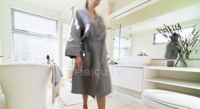 Mulher em roupão de banho por banheira de imersão em ensolarado banheiro moderno — Fotografia de Stock