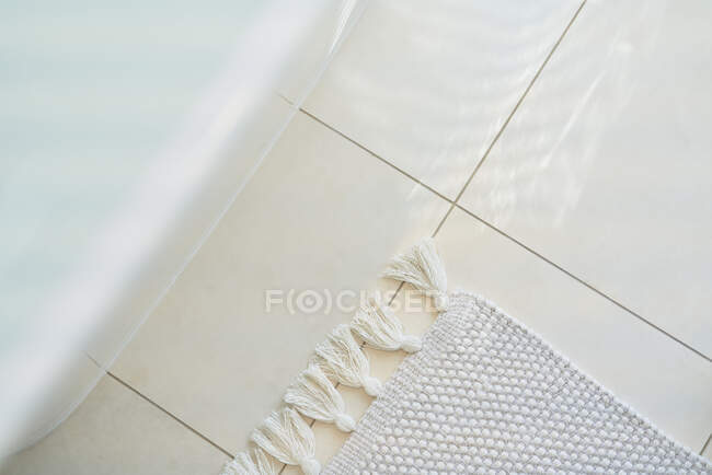 Fringe rug on white tile floor below bathtub in bathroom — Stock Photo