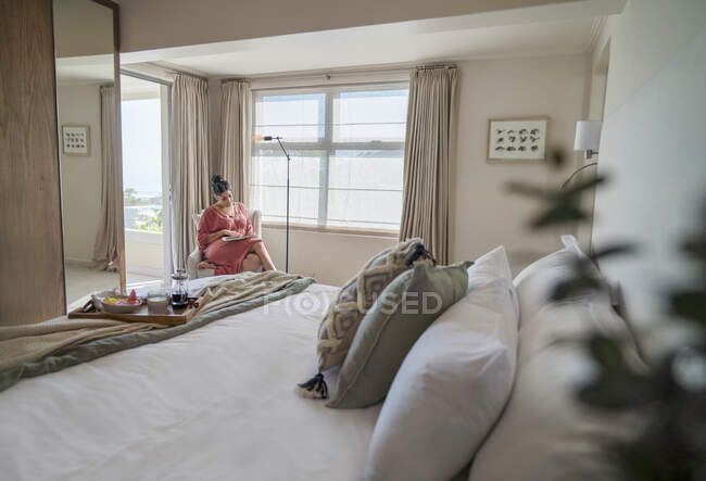Mujer leyendo libro en ventana soleada de la mañana en el dormitorio principal de lujo - foto de stock