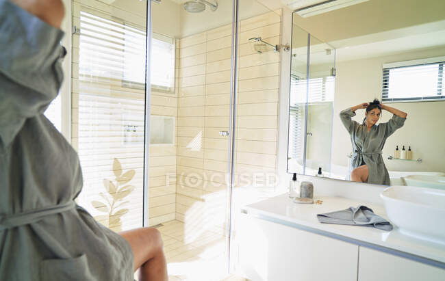 Donna in accappatoio fissaggio capelli nello specchio bagno soleggiato — Foto stock