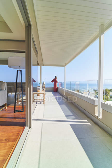 Жінка в довгій сукні на сонячному довгому розкішному балконі з видом на океан — стокове фото