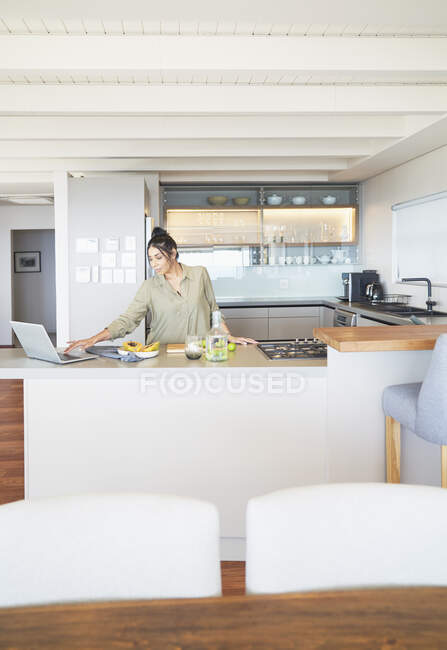 Woman with laptop working and cooking in modern kitchen — Stock Photo