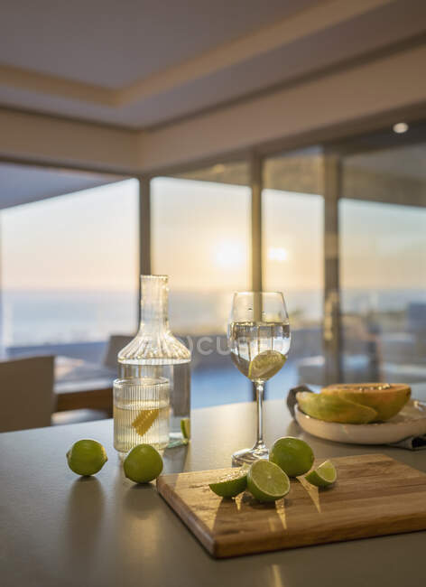 Eau et limes fraîches sur le comptoir de la cuisine au coucher du soleil — Photo de stock