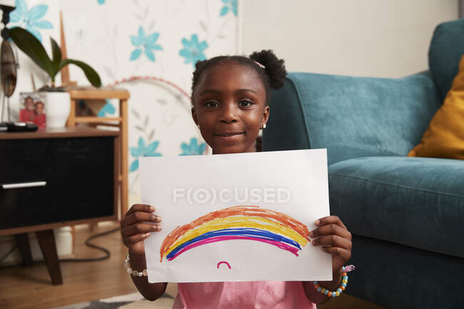 Retrato linda chica sosteniendo el dibujo del arco iris en sala de estar - foto de stock