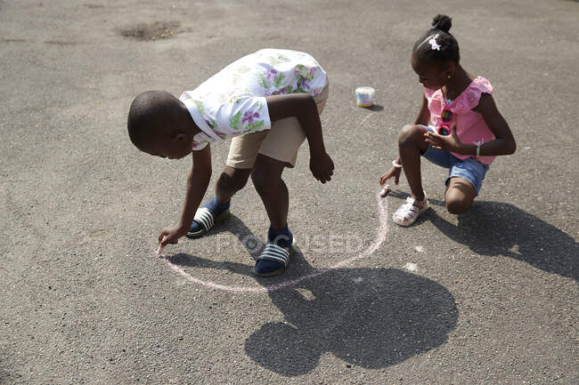Brother and sister playing with sidewalk chalk on sunny pavement — Stock Photo