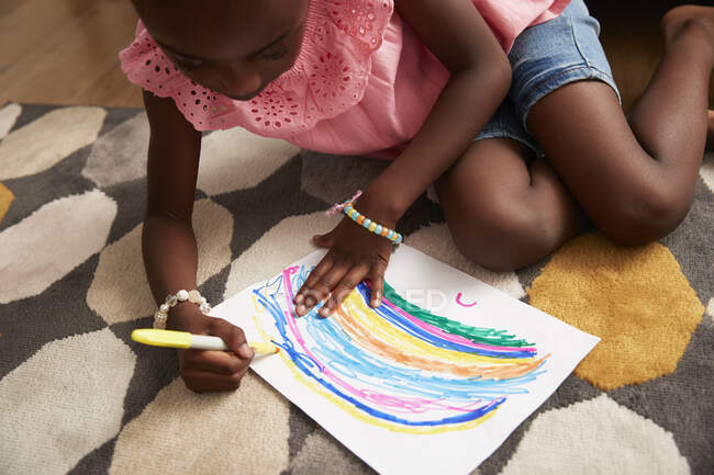 Girl drawing multicolor rainbow with marker on rug — Stock Photo