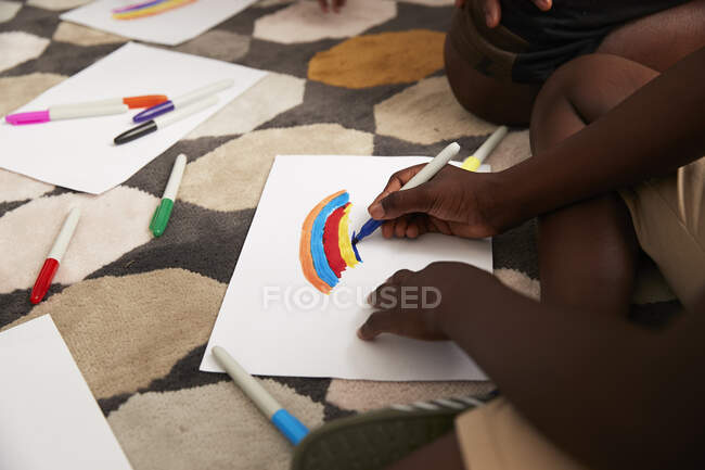 Boy drawing multicolor rainbow with markers on rug — Stock Photo
