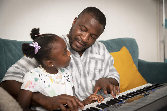 Affectionate father and daughter playing keyboard piano on sofa — Stock Photo
