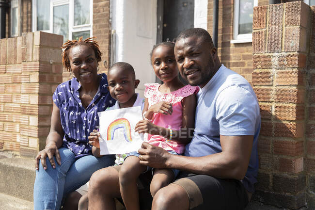 Portrait happy family with rainbow drawing on sunny front stoop — Stock Photo