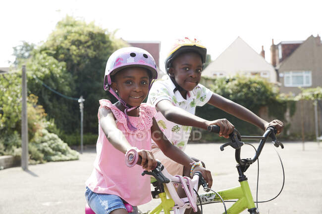 Ritratto felice fratello e sorella in bicicletta nel quartiere soleggiato — Foto stock