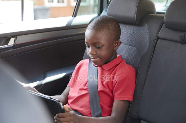 Мальчик с цифровым планшетом на заднем сидении автомобиля — стоковое фото